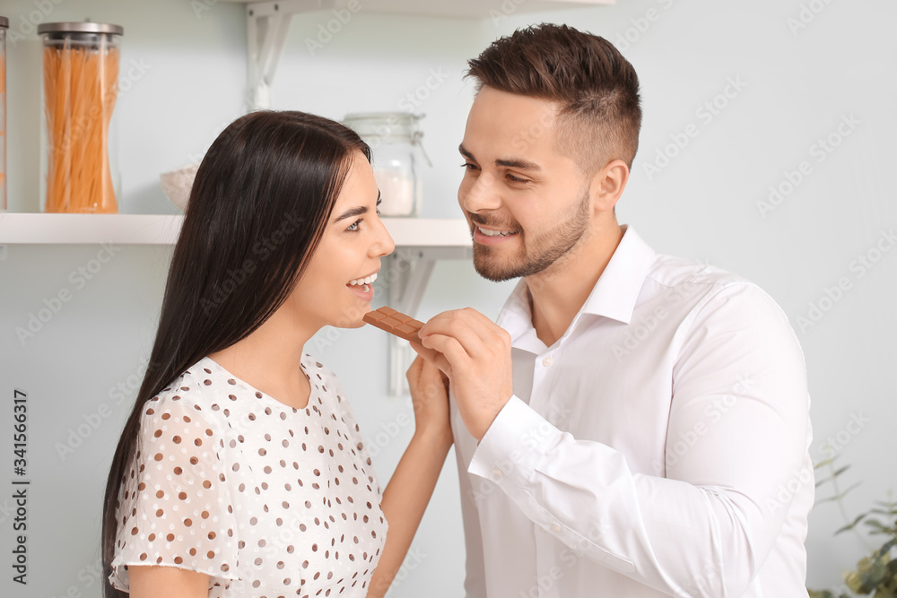 Beautiful young couple eating chocolate in kitchen Beautiful young couple eating chocolate in kitchen