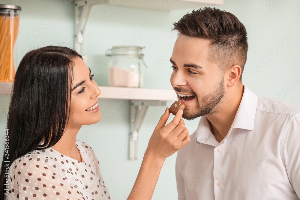 Beautiful young couple eating chocolate in kitchen