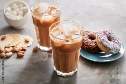 Glasses of tasty iced coffee with sweets on grey background