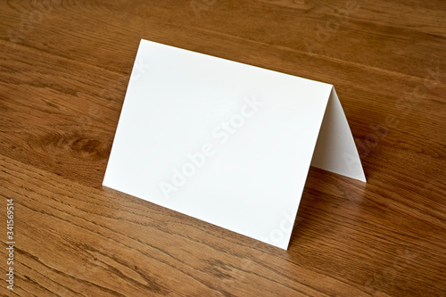 Standing blank empty greeting card mock up on dark wooden background. For use as a Christmas, birthday, wedding or celebration background template.	