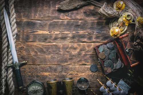 Pirate treasure chest with ancient coins and other various pirate equipment on flat lay table background.