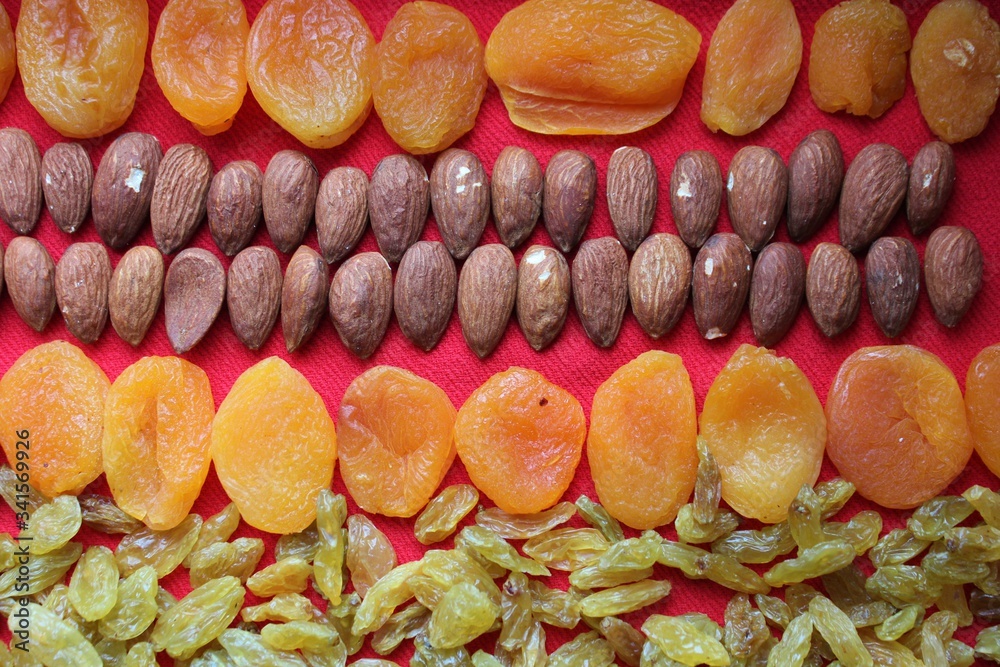 Almonds, raisins and dried apricots laid out by a line on a red background. Almonds, dried apricots and raisins close-up with place for text. Nuts and dried fruits, healthy nutrition.