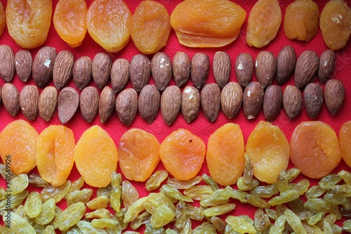 Obraz na płótnie Almonds, raisins and dried apricots laid out by a line on a red background. Almonds, dried apricots and raisins close-up with place for text. Nuts and dried fruits, healthy nutrition. w salonie
