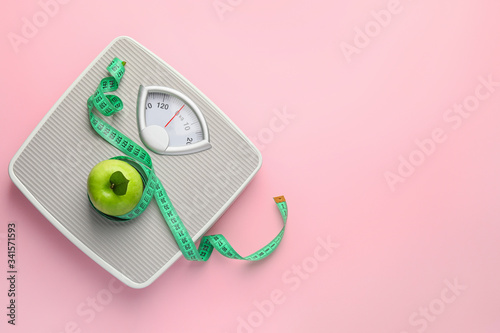 Weight scales with measuring tape and apple on color background. Slimming concept photo