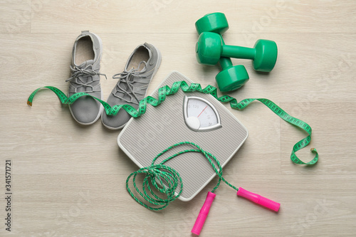 Weight scales with measuring tape, sport shoes and dumbbells on wooden background. Slimming concept
