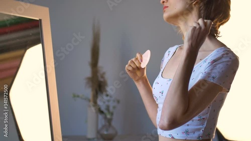 The girl makes a massage gua sha in front of the mirror at home using rose quartz massager, natural stone. Lifting, stimulate lymphatic system and anti age effect