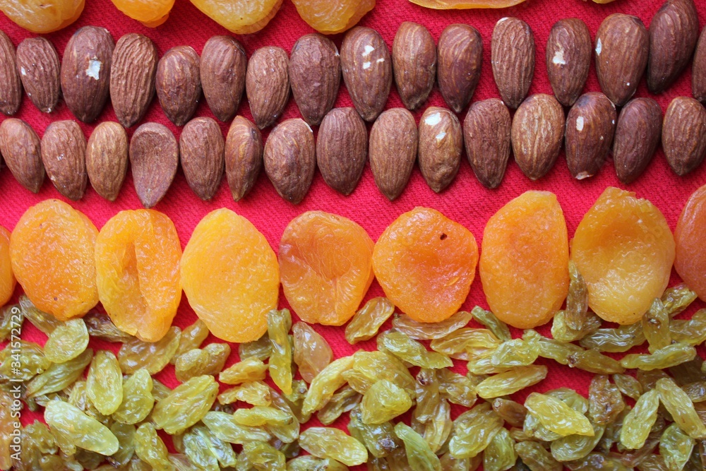 Assortment of nuts,dried fruits and seeds on a wood background.Dried fruits and nuts, symbols of judaic holiday Tu Bishvat. Almonds, raisins and dried apricots laid out by a line on a red background.