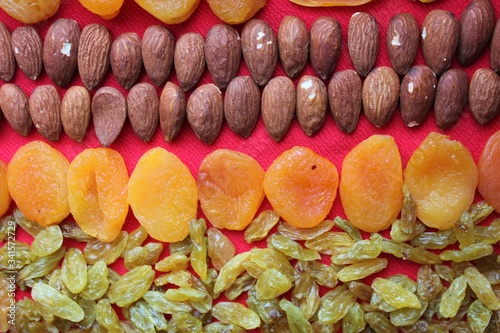 Assortment of nuts,dried fruits and seeds on a wood background.Dried fruits and nuts, symbols of judaic holiday Tu Bishvat. Almonds, raisins and dried apricots laid out by a line on a red background.