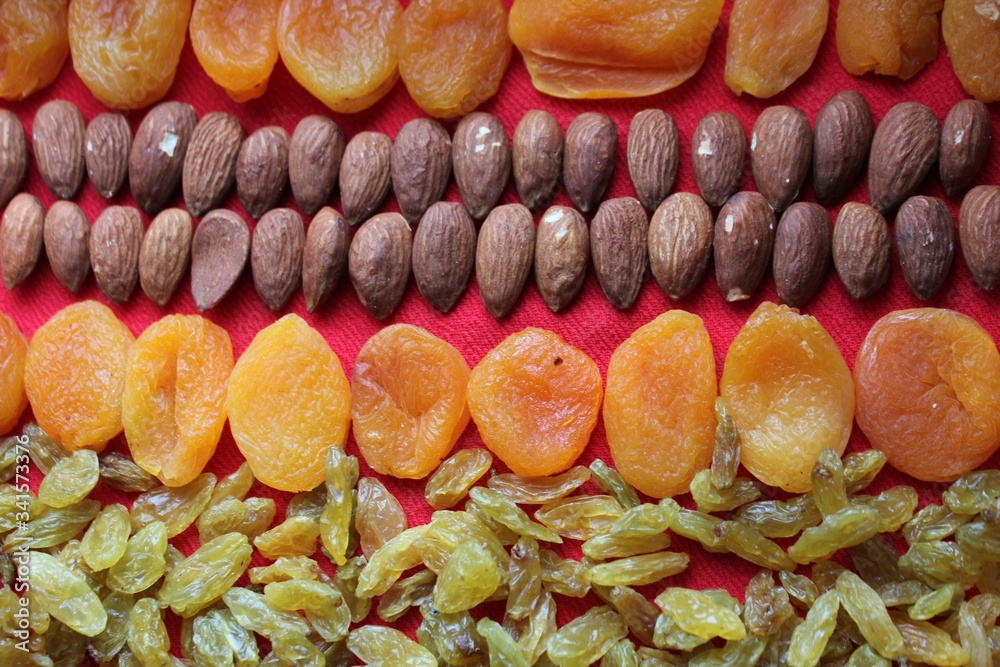 Assortment of nuts,dried fruits and seeds on a wood background.Dried fruits and nuts, symbols of judaic holiday Tu Bishvat. Almonds, raisins and dried apricots laid out by a line on a red background.