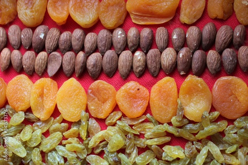 Obraz na płótnie Assortment of nuts,dried fruits and seeds on a wood background.Dried fruits and nuts, symbols of judaic holiday Tu Bishvat. Almonds, raisins and dried apricots laid out by a line on a red background. w salonie