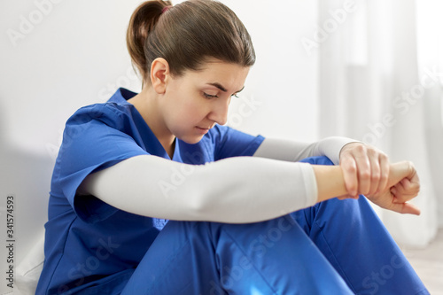 medicine, healthcare and people concept - close up of sad young female doctor or nurse sitting on floor at hospital