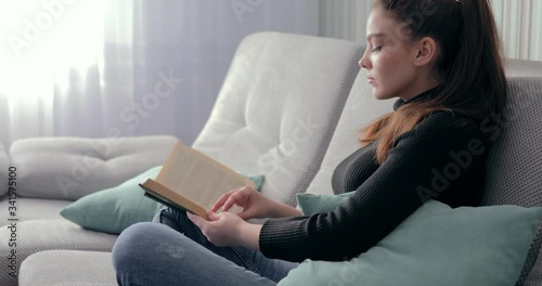 pretty girl reading a book on the couch. stay at home and relax. self development. paper book.