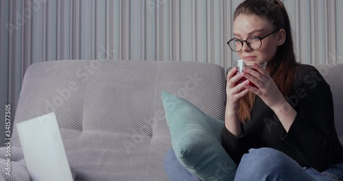 girl working on laptop at home on sofa and drinking tea. stay at home and work remotely. isolation at home.