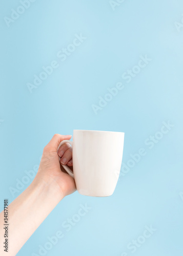 Woman holding white cup on blue background and copy space, vertical. Template mockup mug in hand