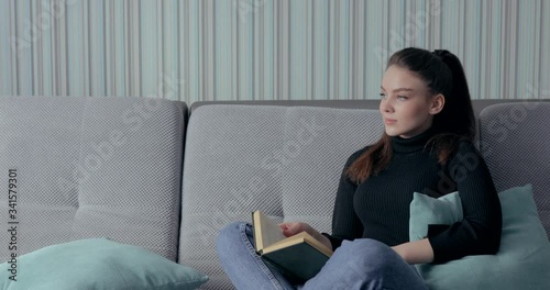 pretty girl reading a book on the couch. stay at home and relax. self development. paper book.