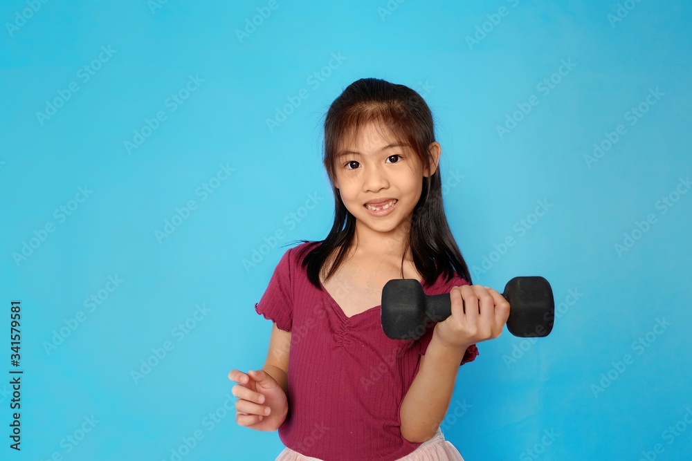 A cute Asian girl holding a dumbbell, exercising, feeling happy and strong. Plain light blue background. A cute Asian girl holding a dumbbell, exercising, feeling happy and strong. Plain light blue background.