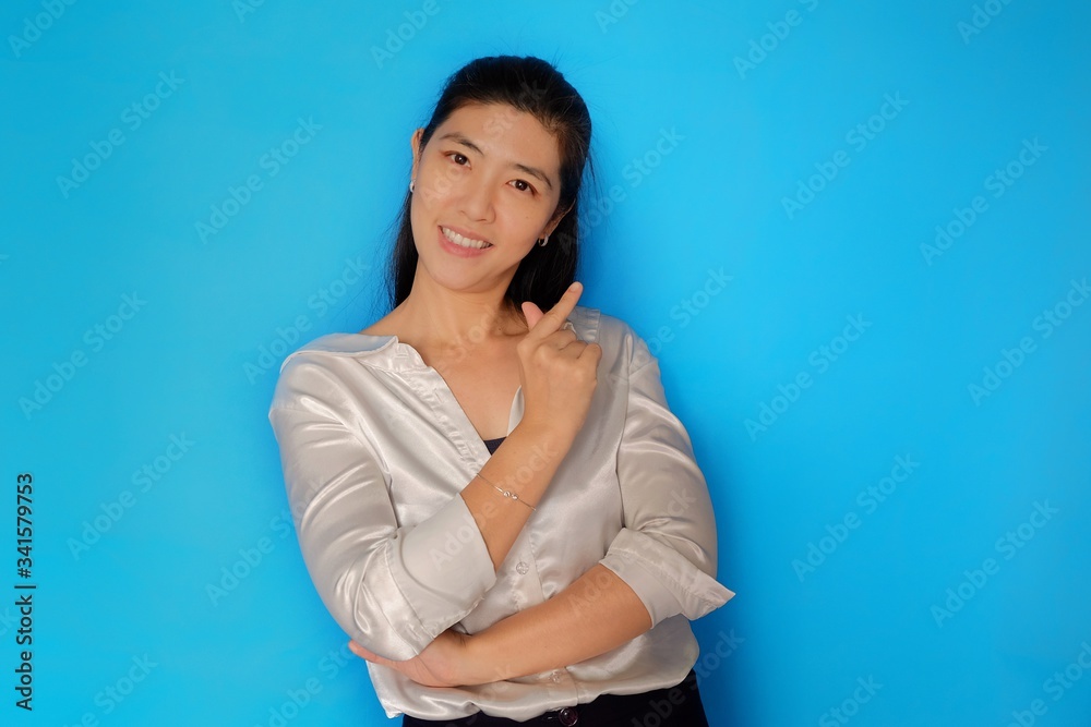 An attractive Asian woman gesturing a mini heart sign with her fingers, smiling and tilting her head slightly. Plain light blue background. An attractive Asian woman gesturing a mini heart sign with her fingers, smiling and tilting her head slightly. Plain light blue background.