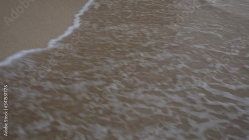 Closeup footage of sea waves washing off footprints on the sandy beach