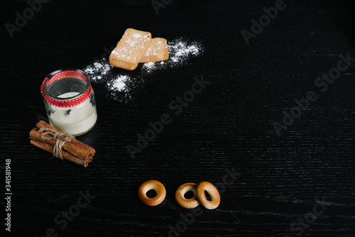 Simple set up for morniing coffee  coffee cup with saucer and few biscuits and bagels plus a bunch of cinnamon sticks. and sugar powder for decoration. black background
