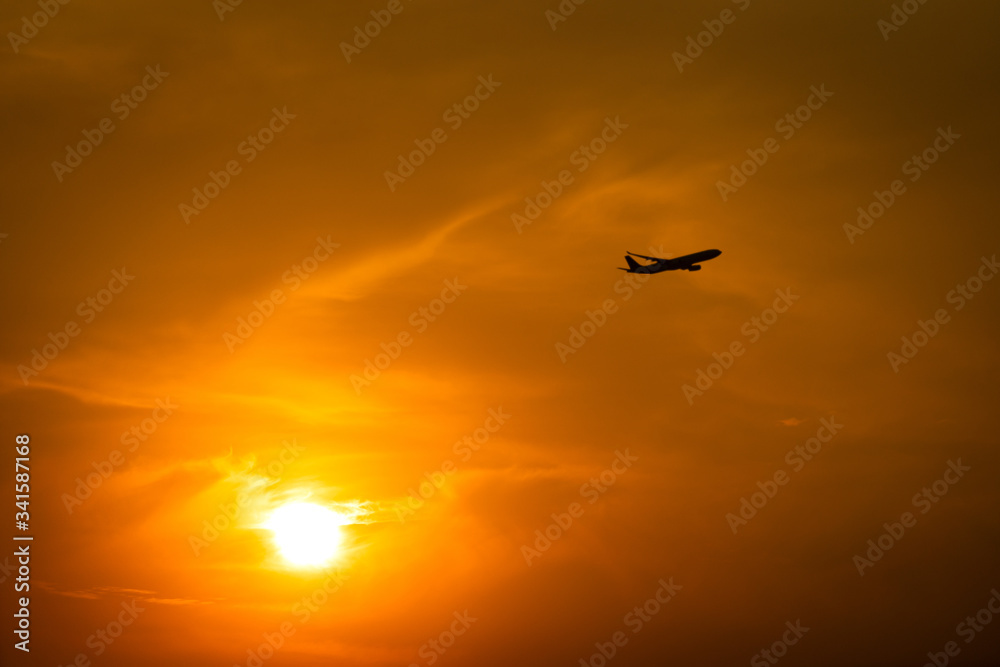 Silhouette photo of Airplane flight during flying in dramatic orange sky and burning sun as background. Travel destination and transportation activity concept.