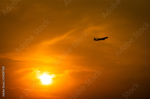 Silhouette photo of Airplane flight during flying in dramatic orange sky and burning sun as background. Travel destination and transportation activity concept.