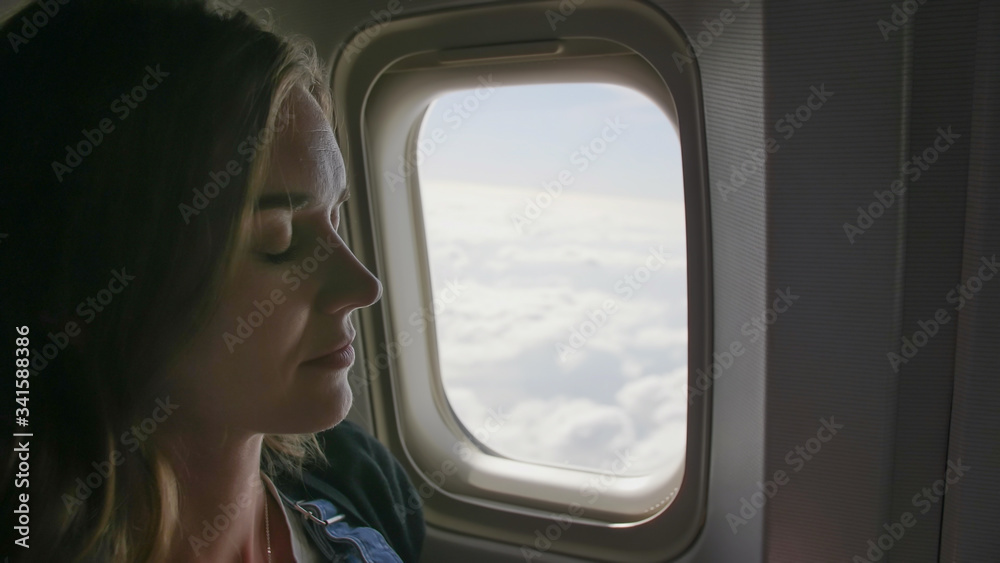A young woman is sleeping at the window of an airplane. A young woman is sleeping at the window of an airplane.