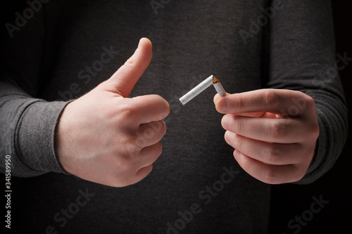 Male holding a broken cigarette and showing thumbs up. Stop smoking cigarettes concept. Quit bad habit  healthy lifestyle concept. No smoking. Do not choose wrong lifestyle.