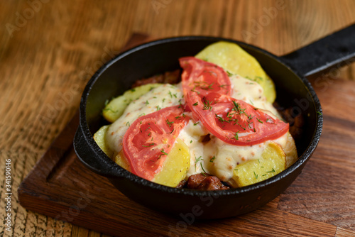 Meat and mushroom gratin with cheese and tomatoes served in a pan over dark wooden table background. Ukrainian cuisine.