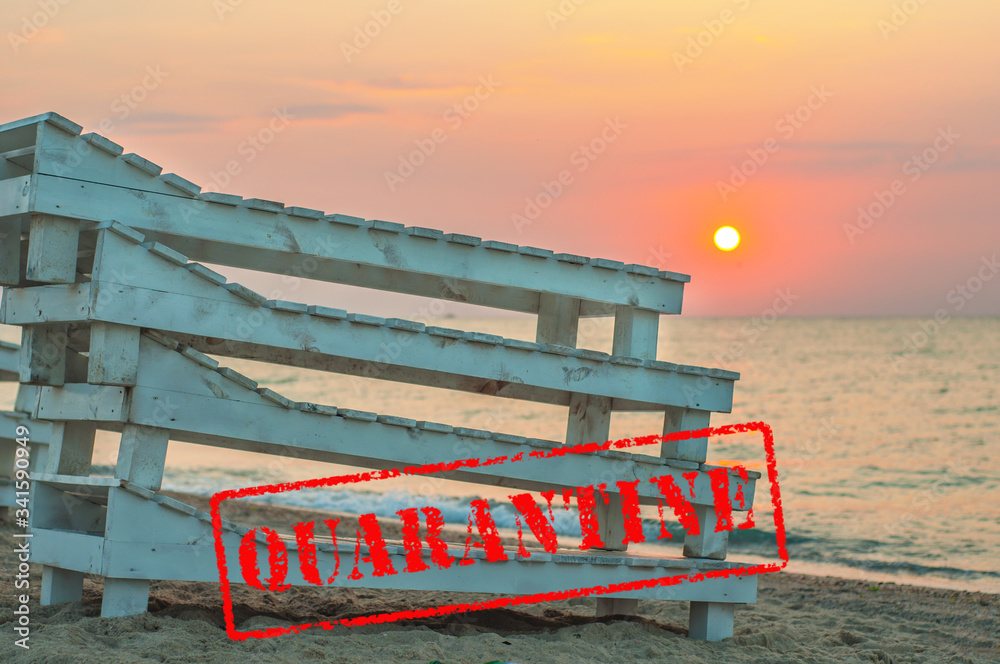 Obraz premium Folded wooden deck chairs on a deserted beach by the sea. Quarantine on summer sea vacation. The failure of the sea season. Coronavirus COVID-19. Red stamp seal QUARANTINE. Closed city public beaches
