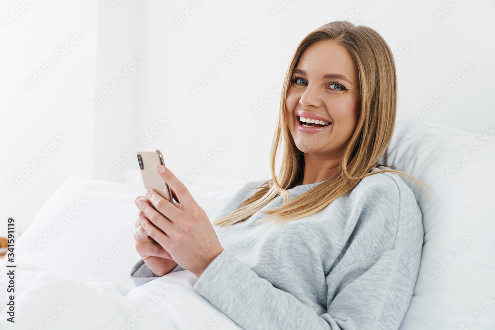 Image of cute joyful woman using cellphone while lying after sleep Image of cute joyful woman using cellphone while lying after sleep