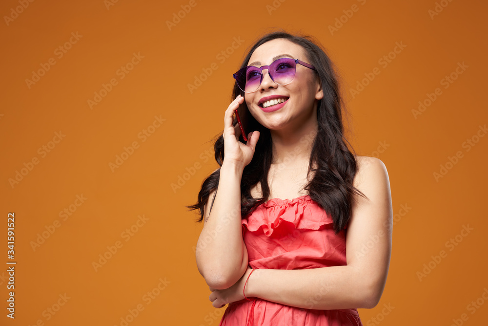 Happy woman in purple glasses talking on phone on empty orange background