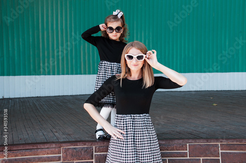 Canvas Print Young beautiful mom with her daughter posing against wall, minimalist street fas