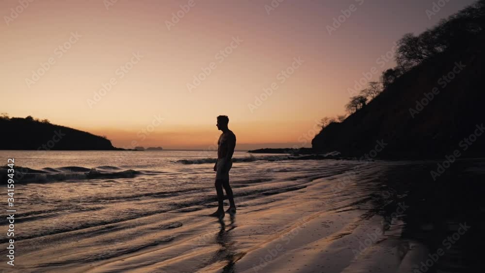 Tamarindo Beach In Costa Rica - A Man Walking By The Wet Sandy Shore In Barefoot With A Beautiful Sunset Background - Pan Wide Shot Tamarindo Beach In Costa Rica - A Man Walking By The Wet Sandy Shore In Barefoot With A Beautiful Sunset Background - Pan Wide Shot