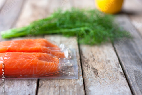 Red fish o salmon fillets in vacuum package on wooden background. Fresh fish, lemon and dill for cooking ingredients. Concept of healthy eating. Omega-3. Selective focus. Close up. Copy space