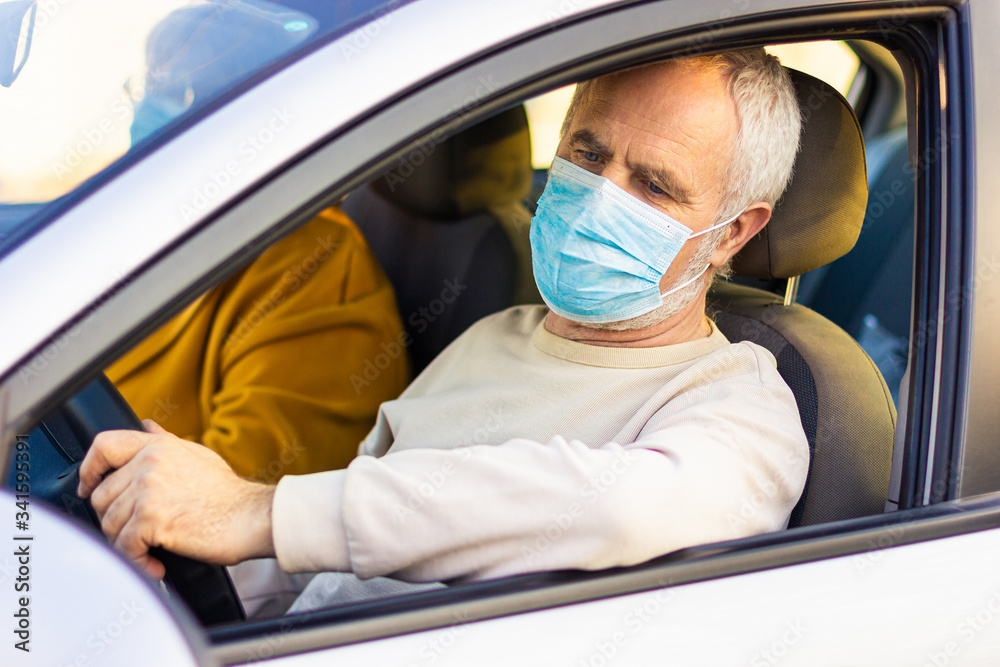Senior man in a medical face mask driving a car. Coronavirus pandemic concept. Road trip, travel and old people concept - happy senior couple driving in car Senior man in a medical face mask driving a car. Coronavirus pandemic concept. Road trip, travel and old people concept - happy senior couple driving in car