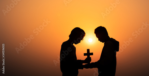 Two young christian holding the cross and praying in morning time with sun light background, Christians should worship and thank God, christian silhouette concept.