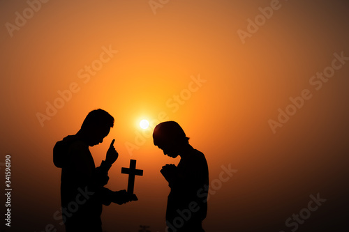 Two young christian worship the God in morning time on the mountain with sun light background, Christians should pray and thank God, christian silhouette concept.