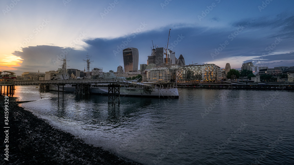 HMS Belfast warship and a view across the River Thames to the financial District buildings in London at sunset, England, Great Britain