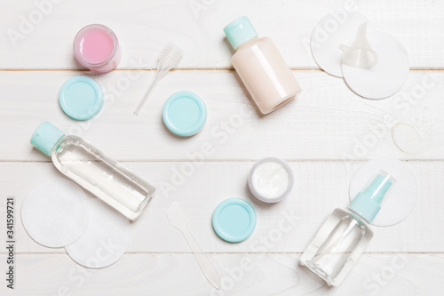Top view of means for face care: bottles and jars of tonic, micellar cleansing water, cream, cotton pads on wooden background. Bodycare concept with empty cpace for your ideas