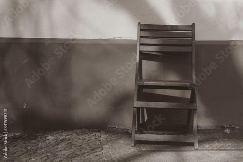 An empty chair standing in front of a house wall, black and white, flat contrast