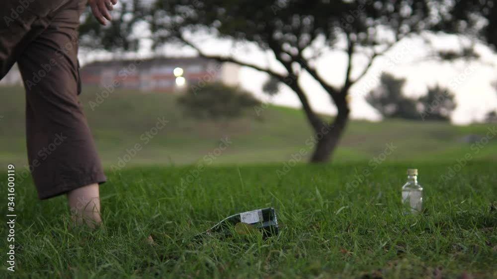Slow-motion shot of a woman walking past, littering in a public park by dumping an empty wine bottle onto the grass. Slow-motion shot of a woman walking past, littering in a public park by dumping an empty wine bottle onto the grass.