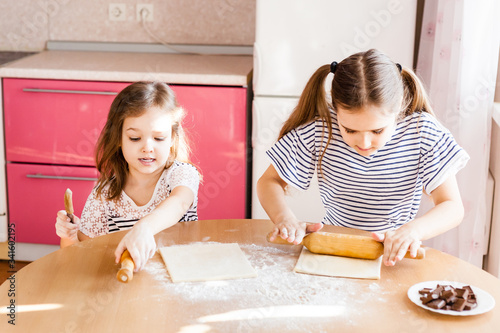 A girl with long hair in a striped T-shirt and a little sister in the kitchen prepare chocolate for baking, flour, plates and a rolling pin for baking, croissants