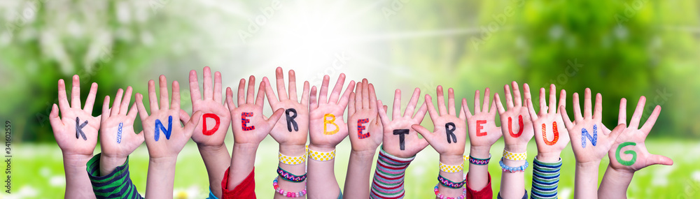 Kids Hands Holding Colorful German Word Kinderbetreuung Means Child Day Care. Sunny Green Grass Meadow As Background - obrazy, fototapety, plakaty 
