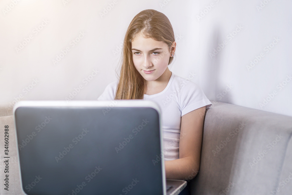 Young girl working on a notebook computer sitting on the bed in the house. distance learning, self education in terms of quarantine Young girl working on a notebook computer sitting on the bed in the house. distance learning, self education in terms of quarantine