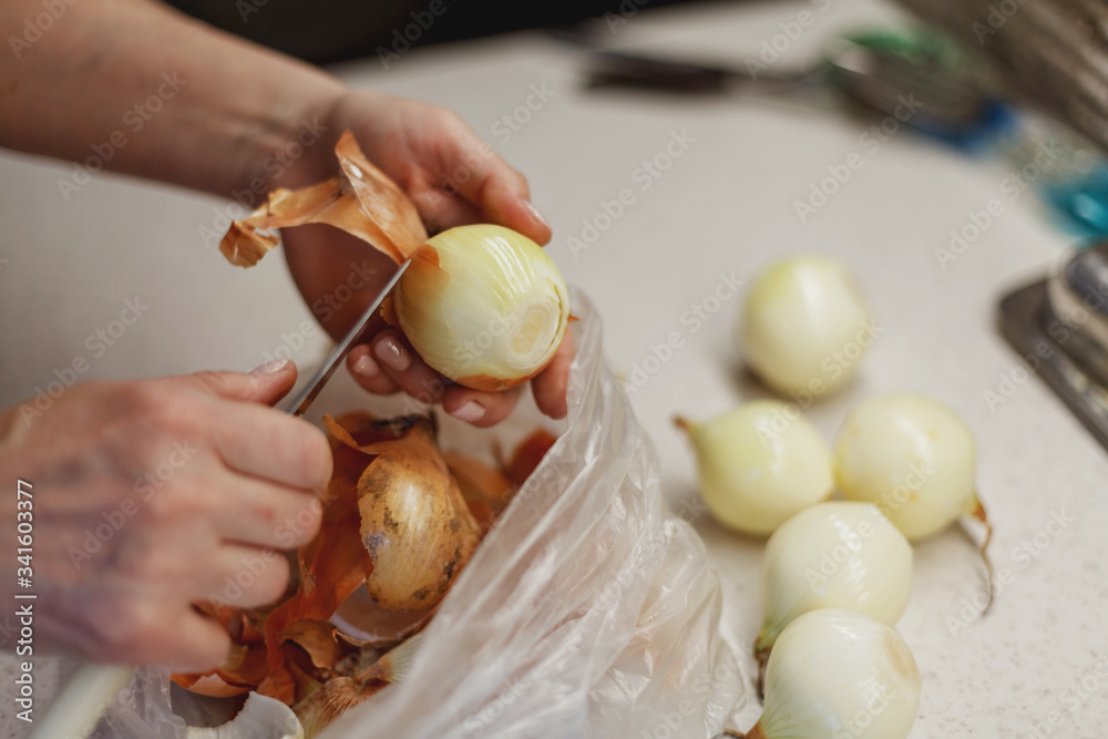 Woman's hands in process of peeling fresh onion above plastic bag