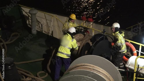 professional oil tanker deck crew arranges large mooring lines rotating black spool under electric light at night photo