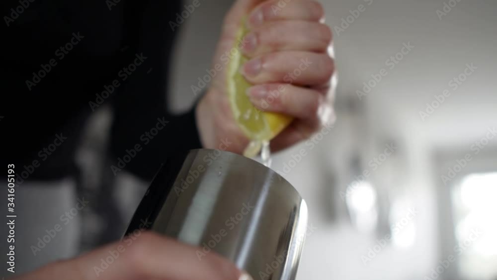 Hand of caucasian female squeezing half of lemon into stainless steel cocktail shaker, RACK FOCUS, SLOW MOTION.