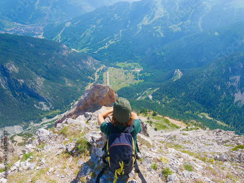 Woman with backpack resting on mountain top, looking at view dramatic landscape valley summer activity fitness wellbeing freedom concept, selective focus rear view