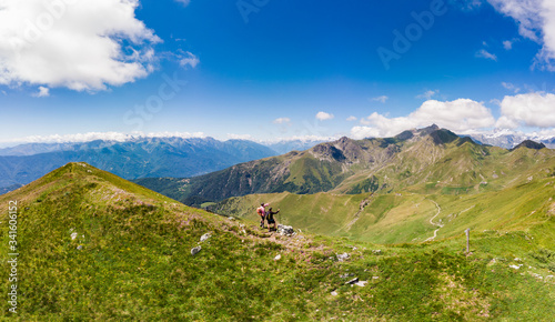 Aerial: couple backpackers hiking on mountain top, scenic landscape. Summer adventures on the Alps. Conquering success mature adult having fun wellbeing fitness