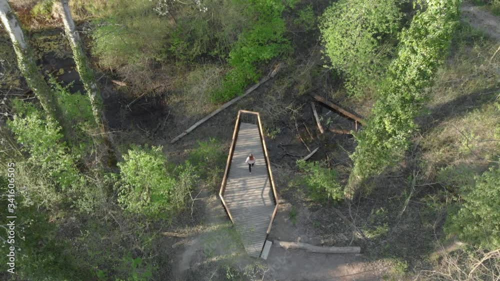 Woman walk alone on a wooden bridge getting lost and suspiciously looking around through the forest. Drone shot horror suspense movie thriller Woman walk alone on a wooden bridge getting lost and suspiciously looking around through the forest. Drone shot horror suspense movie thriller